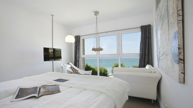 Habitación de hotel con cama, sofá, televisión y una ventana grande con vista al mar.