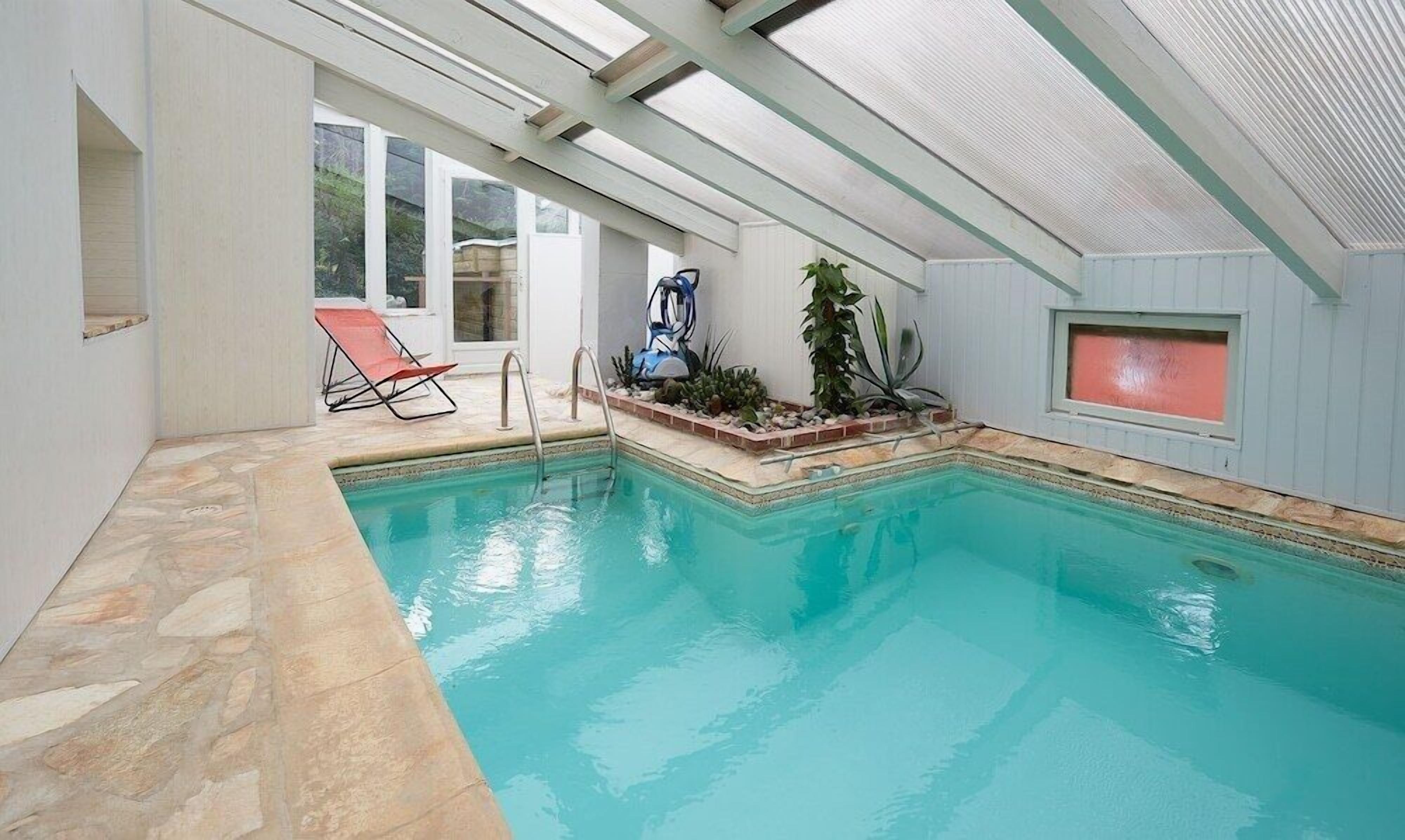 Une piscine intérieure à l’eau claire, une chaise longue et un ventilateur de plafond.