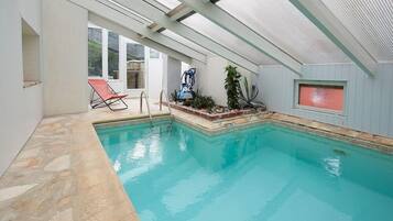 Une piscine intérieure à l’eau claire, une chaise longue et un ventilateur de plafond.