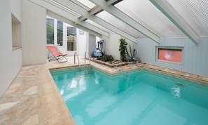 An indoor swimming pool with clear water, a lounge chair, and a ceiling fan. - Hotel The Originals Le Cise (Ault)