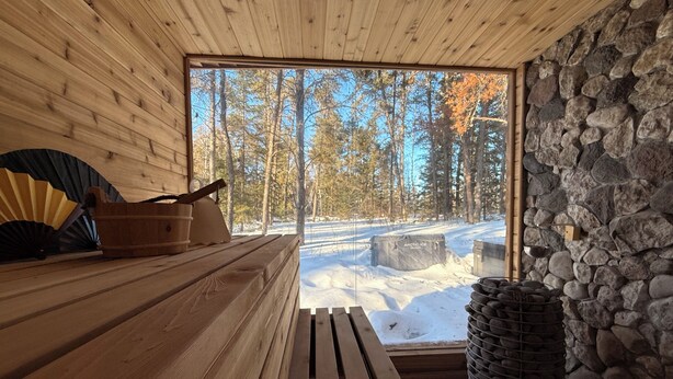Una sauna de madera con pared de piedra y vista a un bosque nevado.