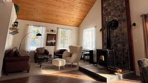 Amplia sala de estar con techo de madera alto, chimenea de piedra y un área de descanso acogedor.