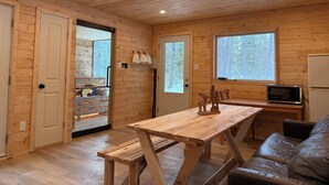 Interior de una cabaña de madera con una mesa de madera, bancos, un sofá, un microondas y un refrigerador.