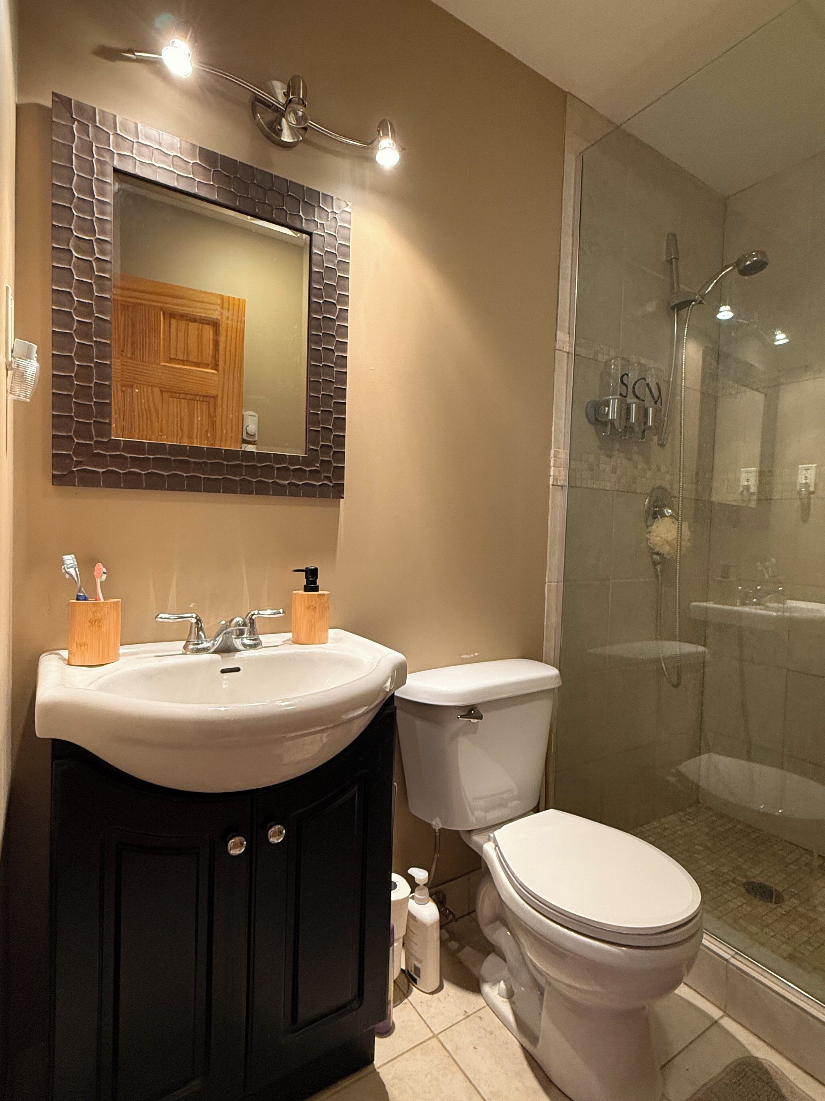 Un baño con lavamanos, espejo, inodoro y ducha.