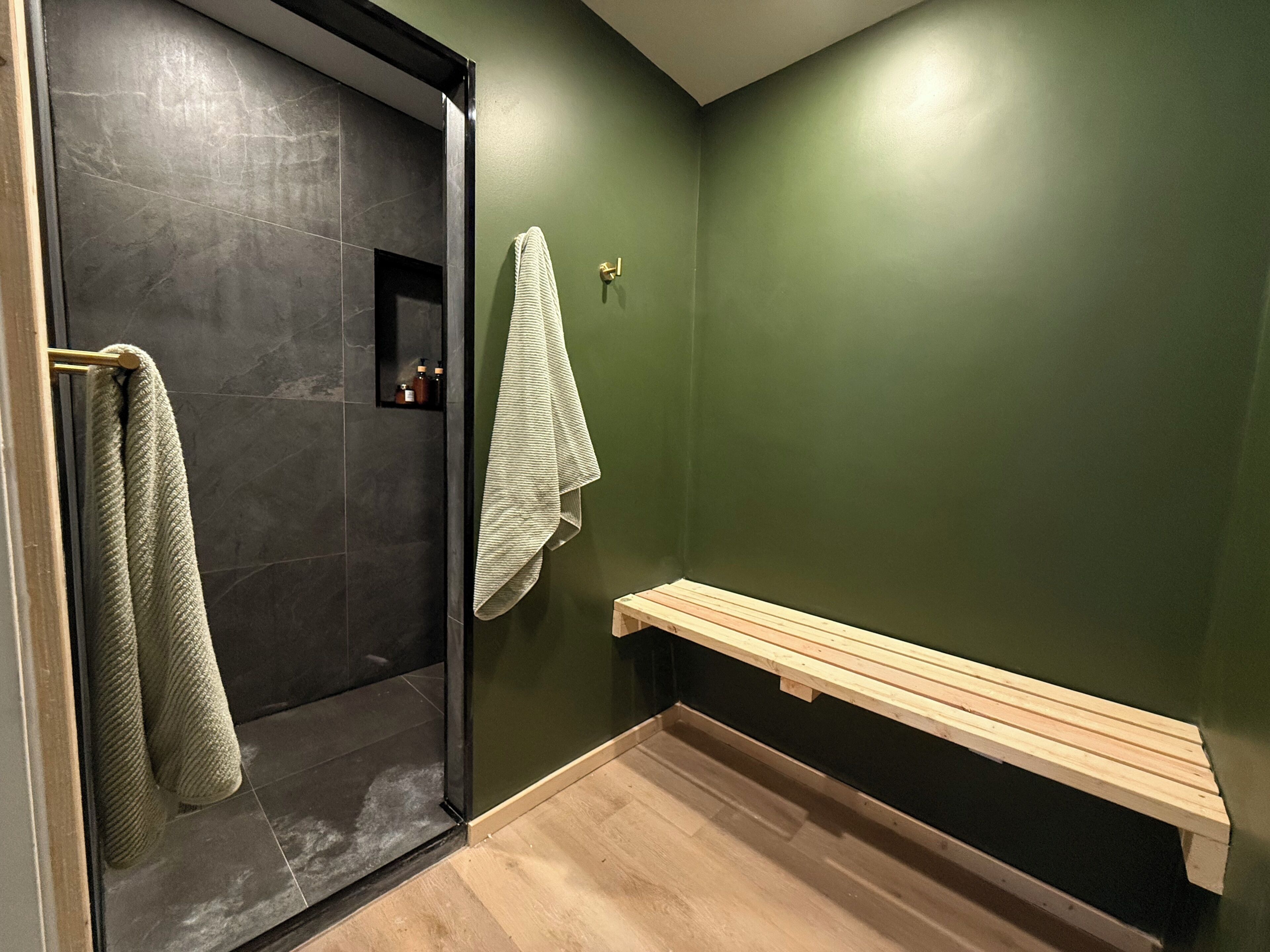 A bathroom with a glass shower door, a wooden bench, and a towel rack.