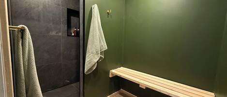 A bathroom with a glass shower door, a wooden bench, and a towel rack.