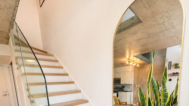 A staircase with glass railings, a potted plant, and a kitchen in the background.