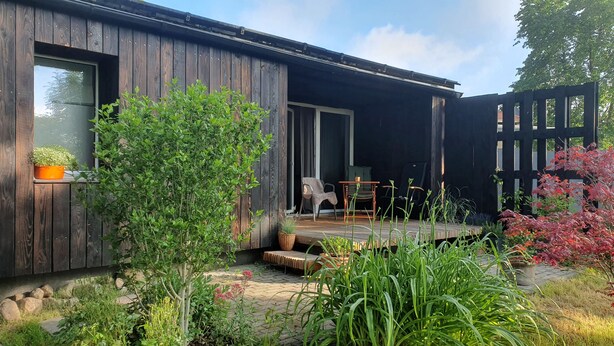 Uma casa de madeira com um pátio, uma cadeira e uma mesa.