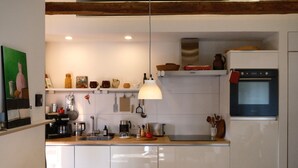 Uma cozinha moderna com armários brancos, forno embutido, cafeteira e luminária pendente.