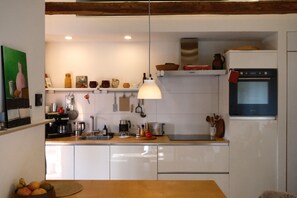 Eine moderne Küche mit weißen Schränken, Backofen, Kaffeemaschine und einer Pendelleuchte.