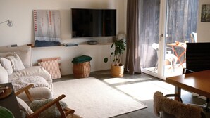 Uma sala de estar com sofá, televisão, mesa de jantar e porta de vidro deslizante para área externa.