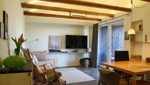 Uma sala de estar com sofá, cadeiras, mesa de jantar, televisão e janela com cortinas.