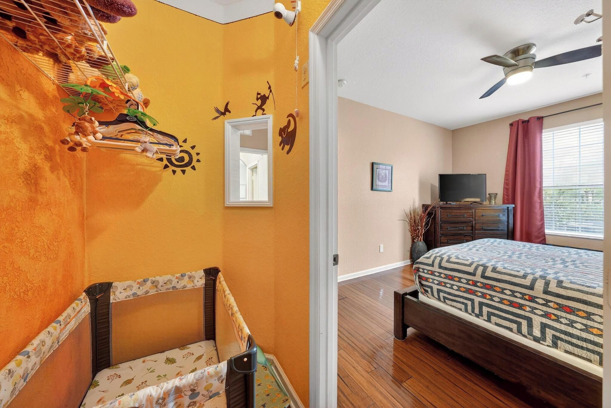 Ett sovrum med en säng, en takfläkt, en tv och ett fönster med gardiner.