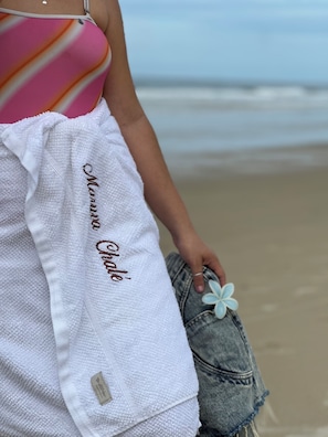 Une personne tenant une serviette blanche sur laquelle est brodé le nom « Marina Cove », et qui se tient sur une plage de sable.