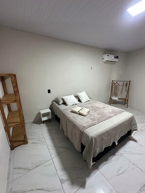 A bedroom with a bed, a wooden ladder, a white nightstand, and a hanging clothes rack.