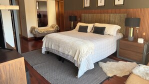 Et moderne hotelværelse med en stor seng, et træhovedgærde, et natbord med lampe og en vægmonteret aircondition.