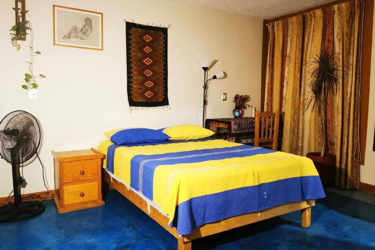 A bedroom with a wooden bed, a bedside table, a fan, a lamp, and a curtain.