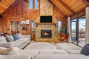 A log cabin interior with a stone fireplace, wooden walls, a sofa, and a television. - Views • Hot Tub • Fenced Yard • Near Downtown (Blue Ridge)