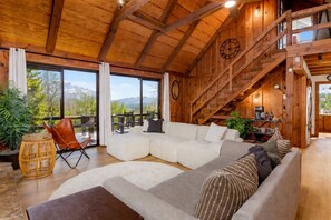 A cozy living room with a sectional sofa, a wicker chair, and a staircase leading to an upper level. - Views • Hot Tub • Fenced Yard • Near Downtown (Blue Ridge)