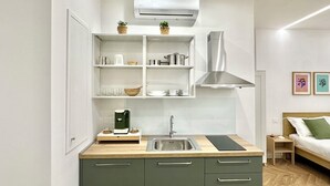 Una kitchenette compacta con un lavamanos, armarios, cafetera y una pequeña encimera.
