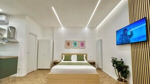 Una habitación de hotel moderna con cama, kitchenette, televisor y una planta en maceta.