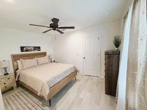 A bedroom with a bed, a ceiling fan, a nightstand, a lamp, a door, and a cabinet. - Hudson Horse Ranch (Hudson)