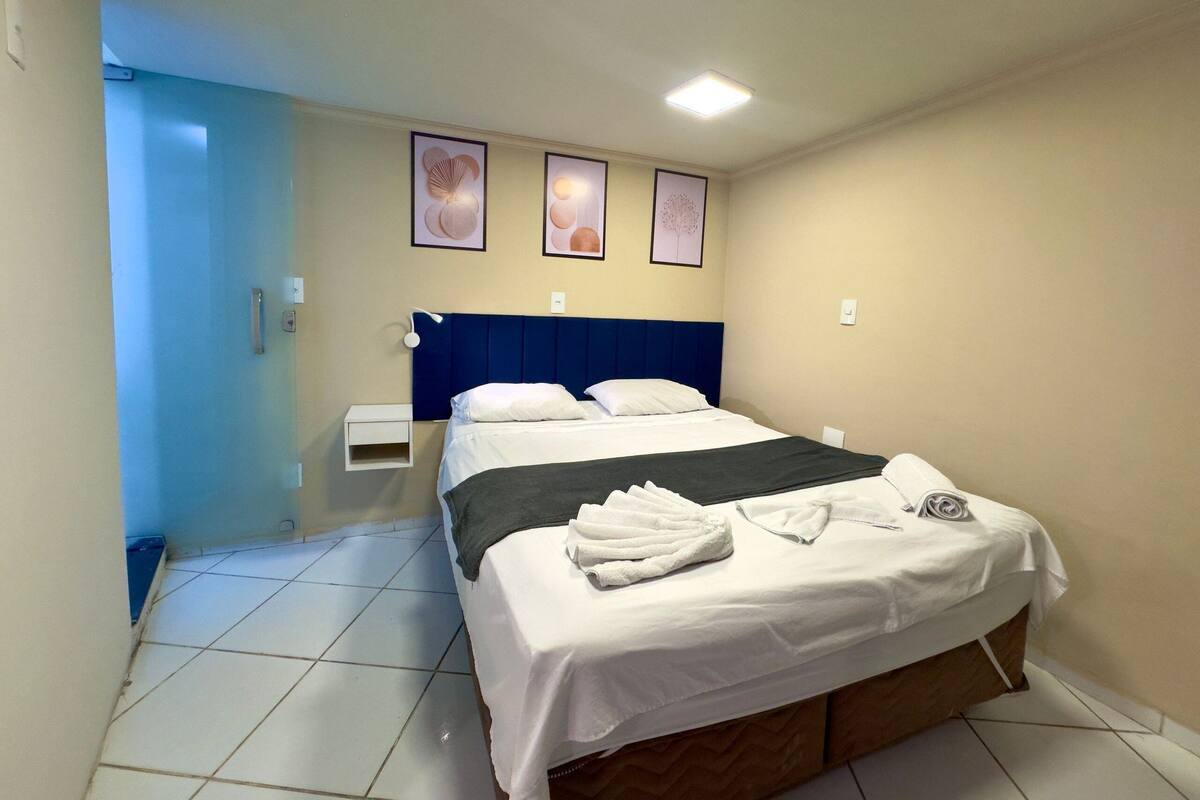 Habitación de hotel con cama, mesita de noche, lámpara de pared y tres cuadros enmarcados.