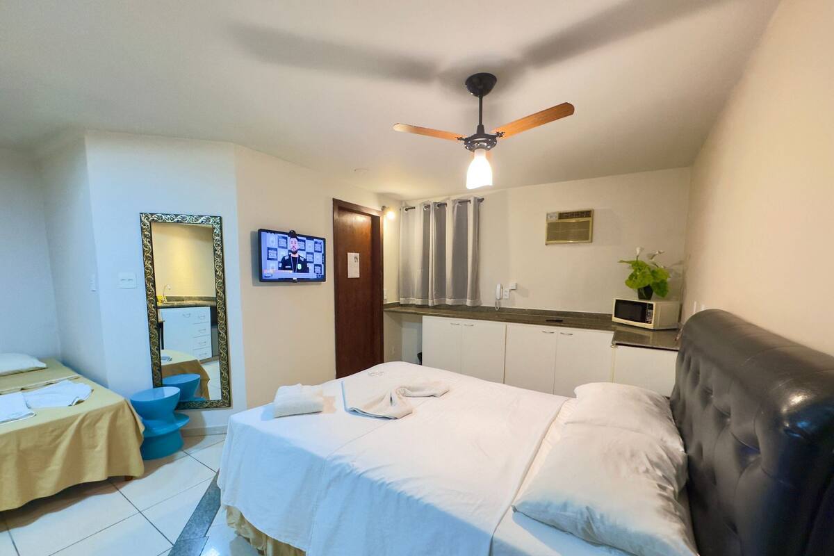 Habitación de hotel con cama, televisión, ventilador de techo, microondas y una planta pequeña.