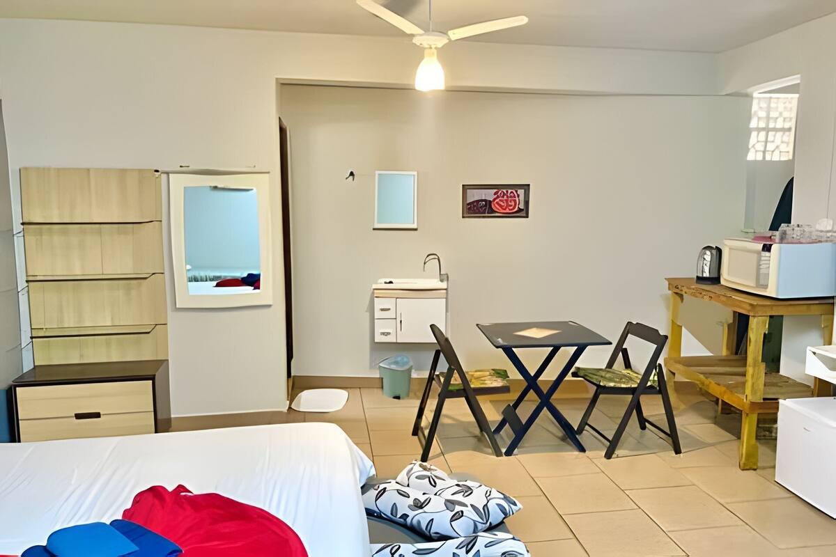 Habitación de hotel compacta con cama, escritorio, silla, lavamanos pequeño y espejo.