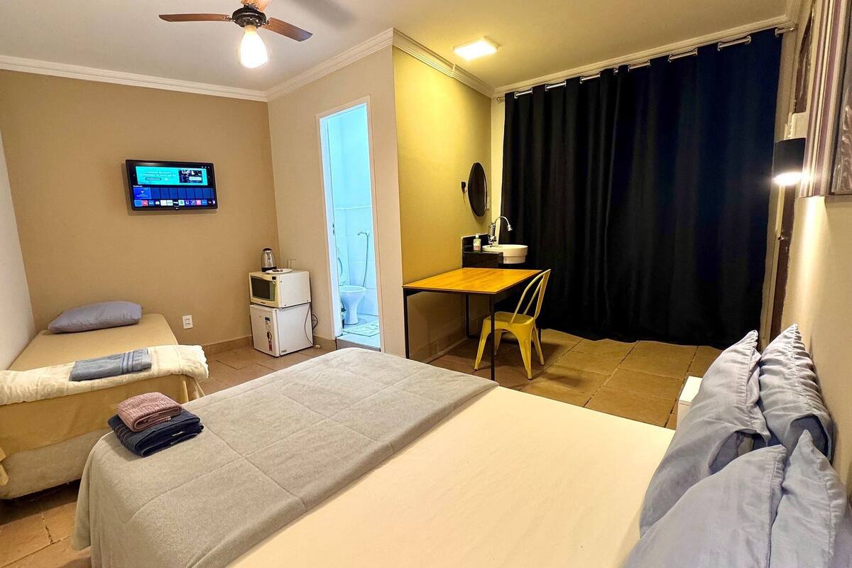 Habitación de hotel con dos camas, un escritorio, un televisor y un baño visible a través de una puerta abierta.
