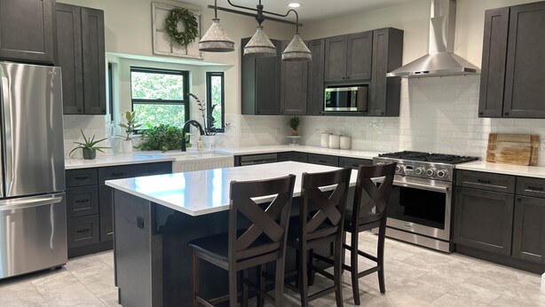 A modern kitchen with dark cabinets, stainless steel appliances, a central island with bar stools, and a large window. - Spacious 4-bedroom, 3-bath, 2-story house in the town of Wellston, Oklahoma (Wellston)