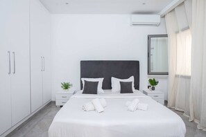 Ein modernes Hotelzimmer mit einem großen Bett, weißen Wänden, einem dunklen Kopfteil und einem Fenster mit Vorhängen.