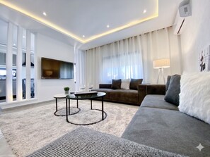 Ein modernes Wohnzimmer mit einer Couch, einem Couchtisch, einem Fernseher und einem Fenster mit Vorhängen.