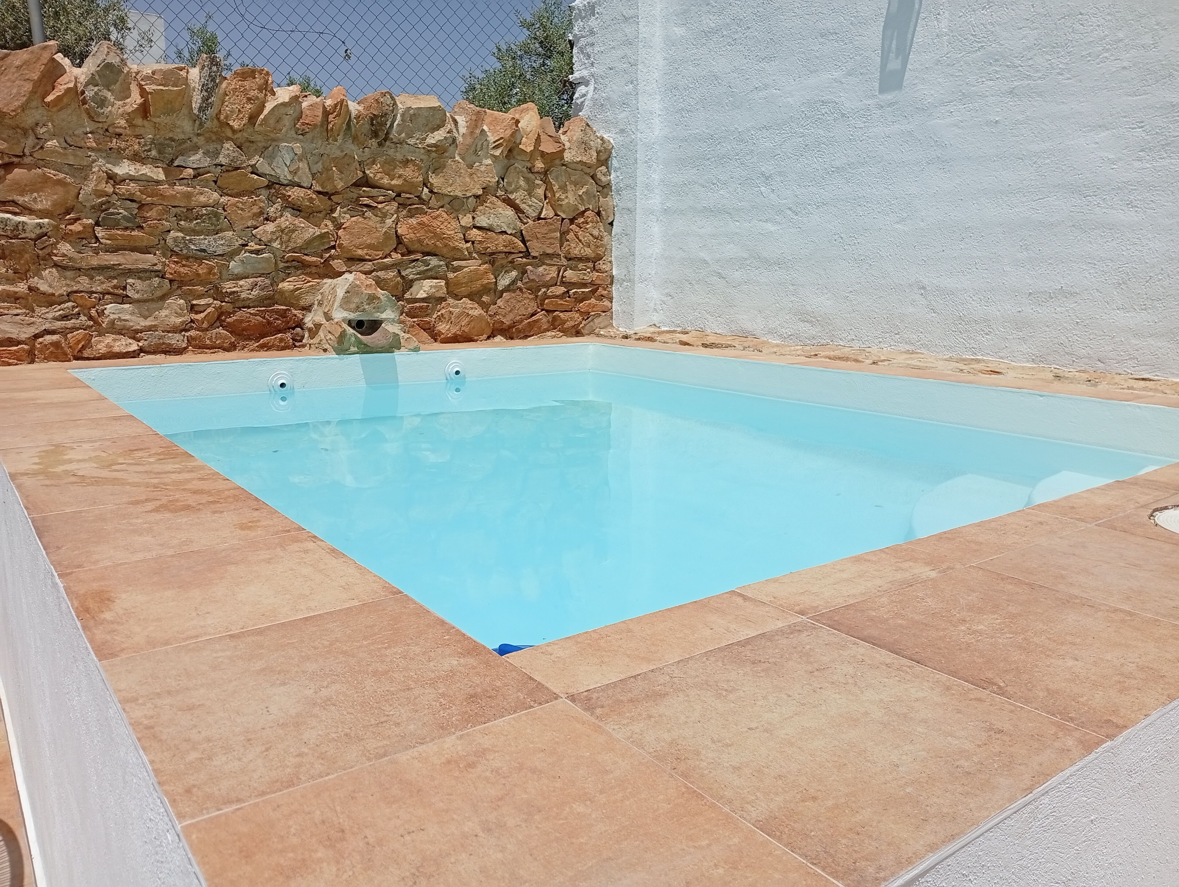A rectangular swimming pool with a stone wall and white wall in the background.