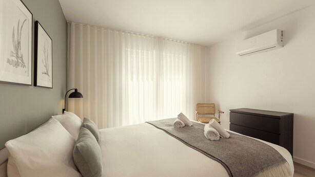 A bedroom with a bed, a bedside table, a chair, a wardrobe, and an air conditioning unit. - Casa Jacinto 9 - City Center (Caldas da Rainha)