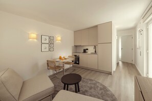 Eine moderne Wohnung mit Essbereich, Küchenzeile und Wohnbereich inklusive Sofa und rundem Tisch.
