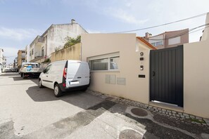 Eine Wohnstraße mit einem weißen Lieferwagen, der an einer beigefarbenen Mauer und einem schwarzen Tor geparkt ist, sowie einem Gebäude mit der Nummer 9.