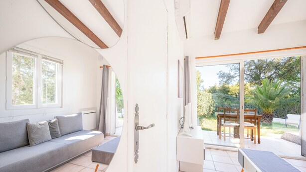 Un interior modern amb un sofà, una banca, una console blanca i una porta corredissa de vidre que dona a una zona exterior amb joc de menjador.