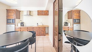 Cuina amb armaris de fusta, microones, rentapeus i zona de dinar amb taula i cadires.