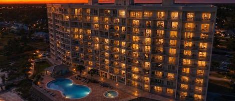 Un hotel de varios pisos con zona de piscina, rodeado por un jardín ajardinado.