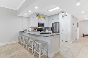 A modern kitchen with white cabinetry, stainless steel appliances, and a central island with bar stools. - HP301 Waterfront Views, Pool, Hot Tub & Dock (Pensacola)
