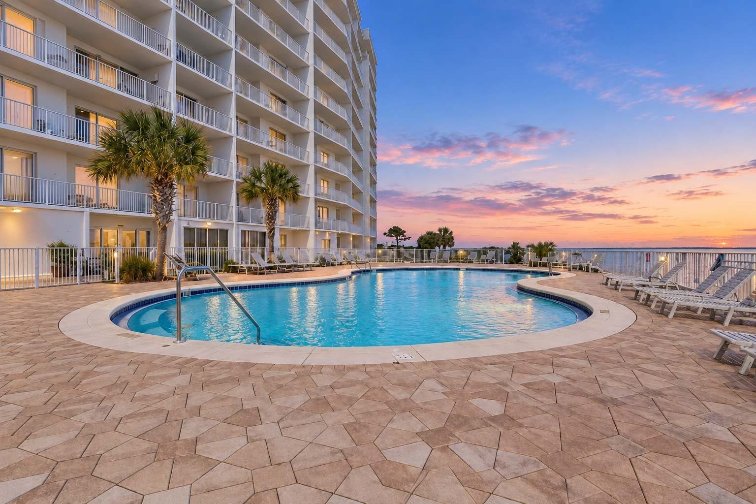 Un hôtel doté d’une piscine, de palmiers et offrant une vue sur le coucher de soleil.