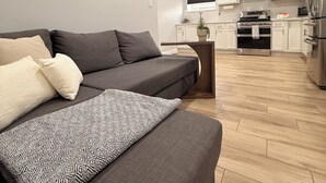 A modern living room with a sofa, a patterned throw pillow, and a cityscape painting on the wall.