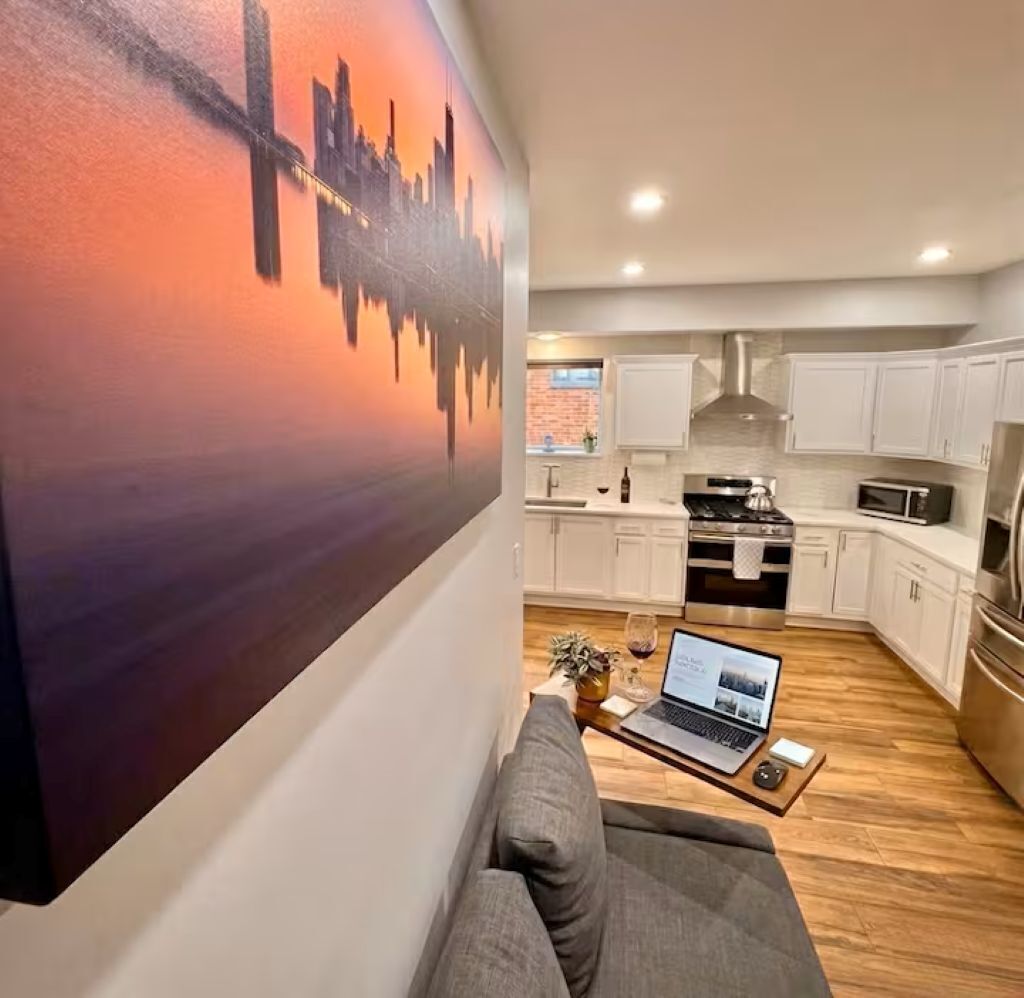 A modern living room with a sofa, a laptop on a coffee table, and a cityscape painting on the wall.