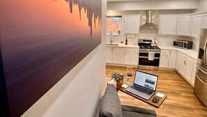 A modern living room with a sofa, a laptop on a coffee table, and a cityscape painting on the wall.