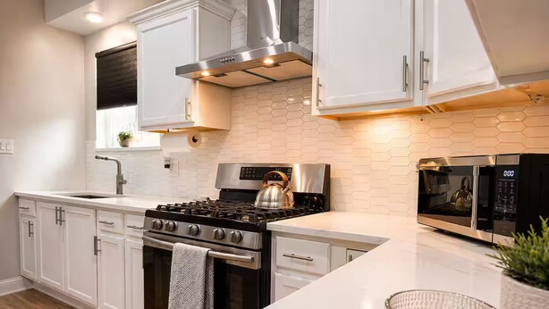 A modern kitchen with white cabinetry, stainless steel appliances, and a wooden countertop.