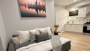 A modern living room with a sofa, a cityscape painting, and a kitchen in the background.