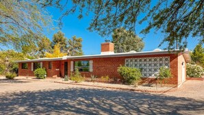 A single-story brick house with a front porch, a garage, and a small garden area. - Mid-Century Oasis w/ heated Pool (Tucson)