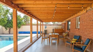 A covered patio with a pool, wooden furniture, and brick walls. - Mid-Century Oasis w/ heated Pool (Tucson)