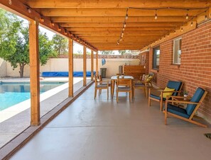 A covered patio with a pool, wooden furniture, and brick walls. - Mid-Century Oasis w/ heated Pool (Tucson)